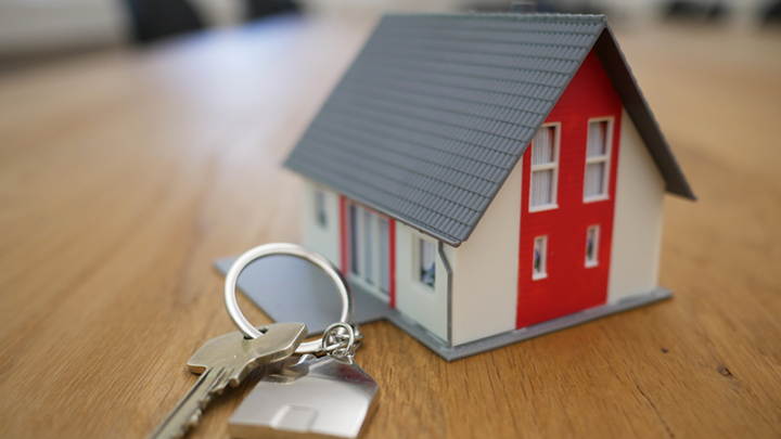 A close-up of a set of house keys next to a miniature house. 