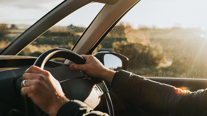A Pair of hands on a steering wheel driving on a sunny day. 