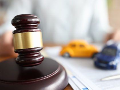 A closeup of a gavel with two model cars in the background. 