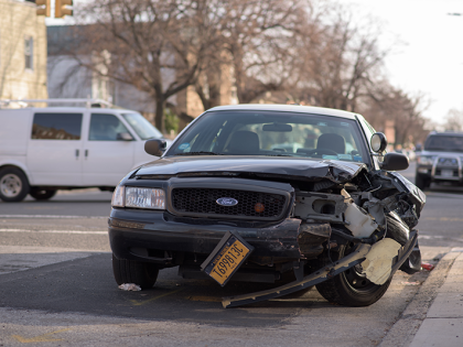 A black sedan car with the front driver side bumper and wheel mangled from an accident. 