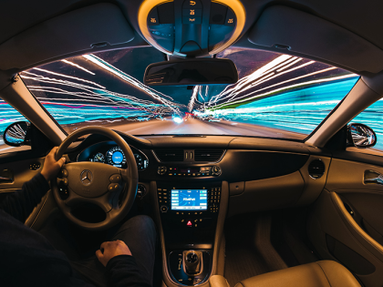 Point of view image of a person driving a car. Lights seem to be zipping by the windows and the windshield, indicating that the car is moving fast.