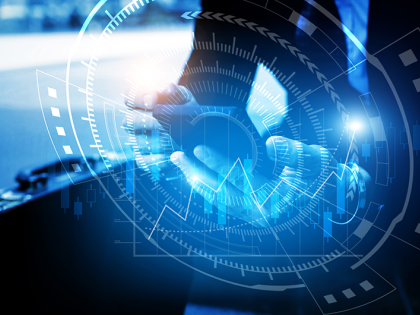 A business man sitting and holding a smart phone next to a briefcase. A blue hologram of stock market charts is overlaid on top of the image.