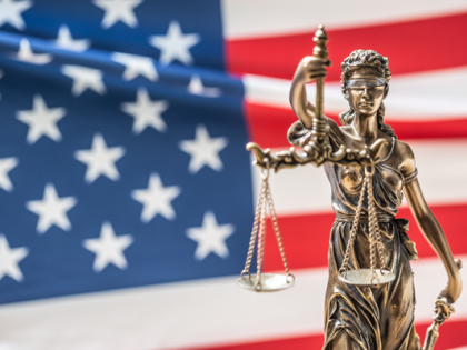 A statue of Lady Justice holding her scales in front of a flowing American flag.
