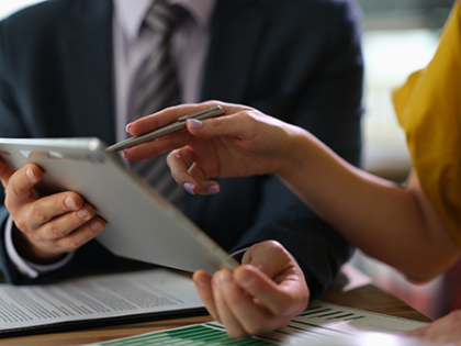 An insurance agent and a client examine contracts and documents on an iPad and on papers on a desk in front of them.