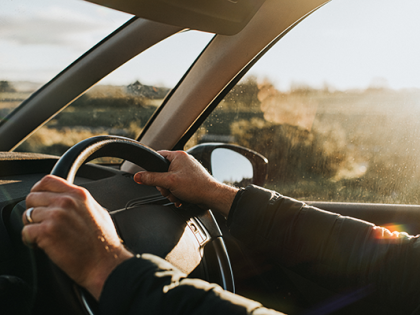 A Pair of hands on a steering wheel driving on a sunny day.